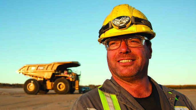 employee in oil sands field with mine truck in background