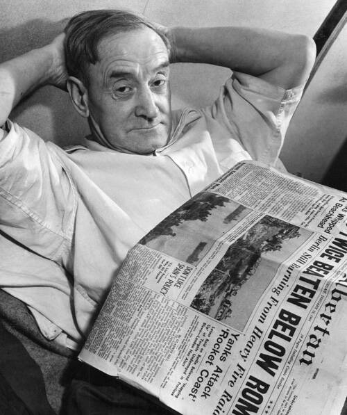 Imperial Oil worker relaxing and reading a newspaper on his bunk in men's quarters, Norman Wells, Northwest Territories